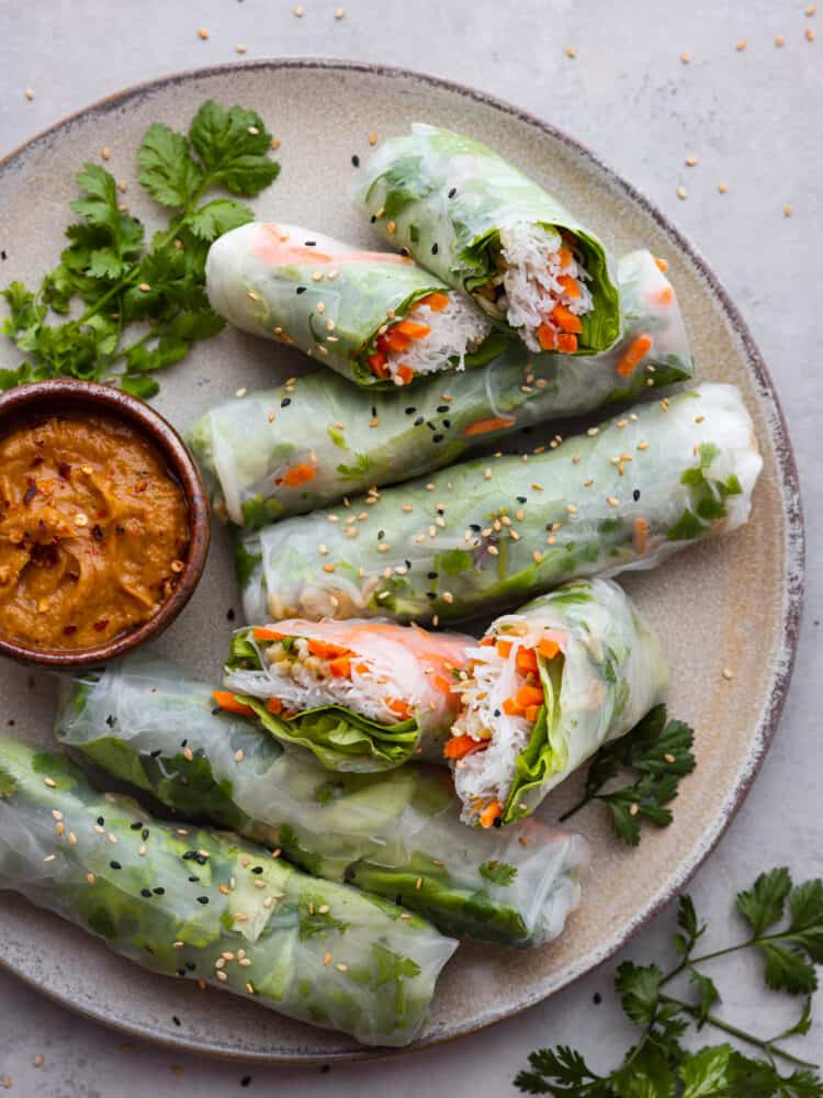 Vietnamese summer rolls served on a gray stoneware plate alongside peanut sauce for dipping.