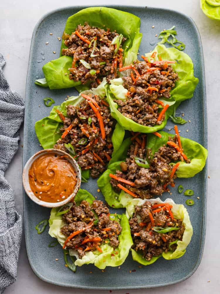 6 Thai lettuce wraps on a blue dish, served with peanut sauce.