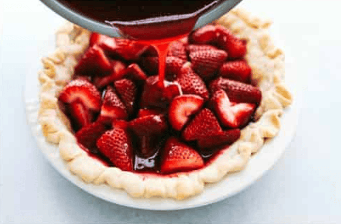 My fresh strawberry pie is one of those desserts that looks gorgeous but is so easy to make. A premade pie crust, juicy, fresh strawberries, and a quick homemade glaze come together to make a glossy, beautiful pie! Pouring the strawberry glaze over the fresh strawberries in the pie crust.