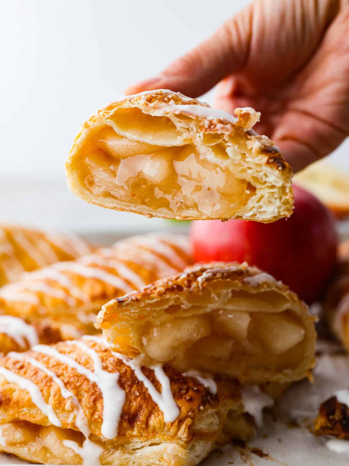 A hand holding an apple turnover that is cut in half. 