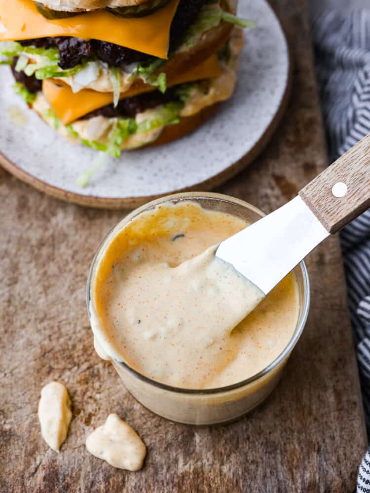 Hero image of Big Mac sauce in a glass container. There is a burger in the background.