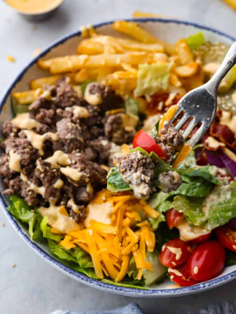 Closeup of lettuce, a halved tomato, and ground beef on a fork.