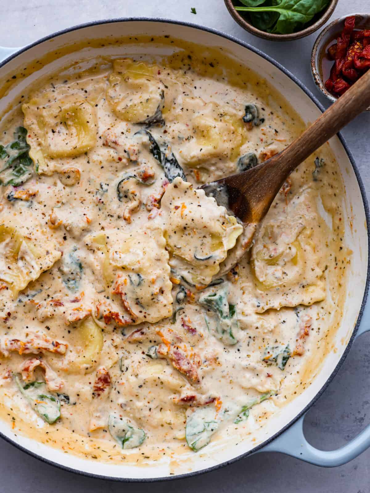 Top-down view of creamy Tuscan ravioli  in a blue and white skillet.