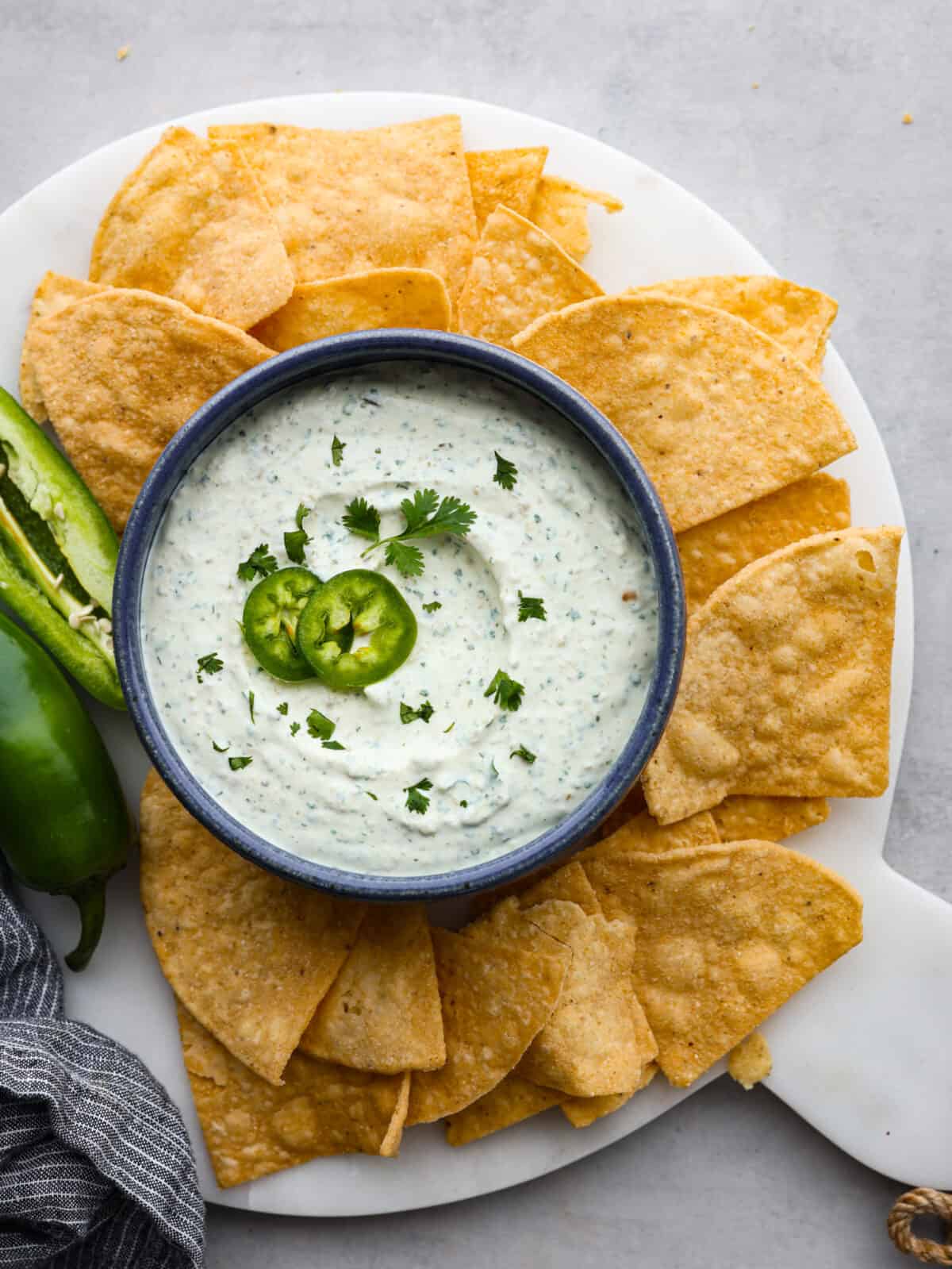 The top view of a platter of tortilla chips with a bowl of jalapeño dip with a sliced jalapeño garnishing the dip. 