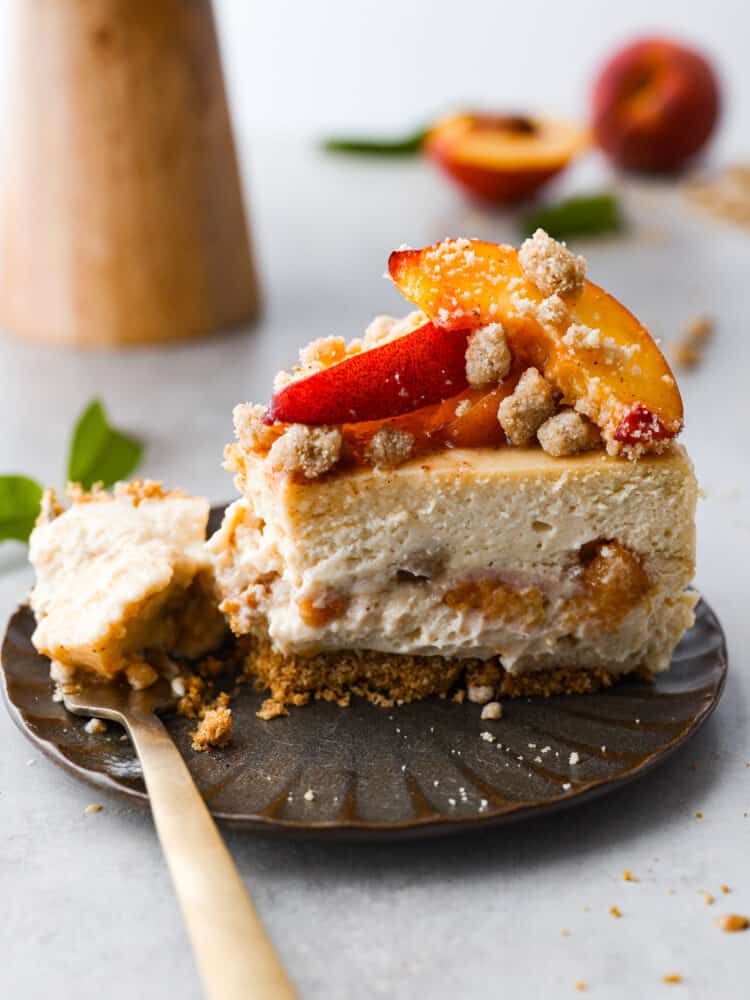 A slice of peach cobbler cheesecake on a brown plate with a gold fork. 