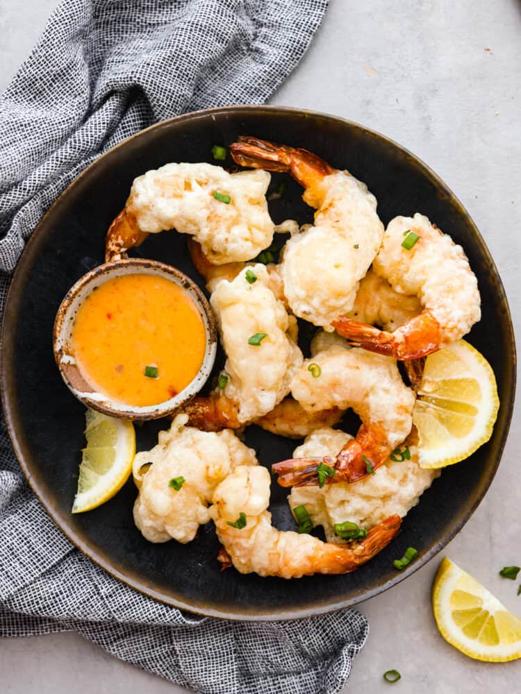 Shrimp tempura served in a brown bowl and served with a small cup of sriracha mayonnaise.