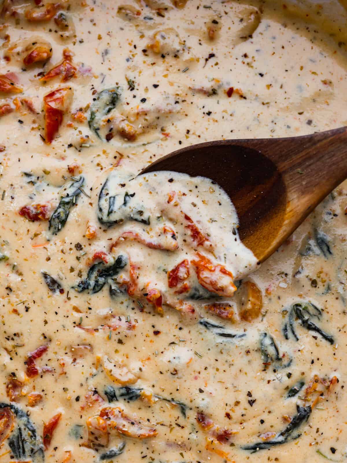 Mixing creamy Tuscan garlic sauce with a wooden spoon.