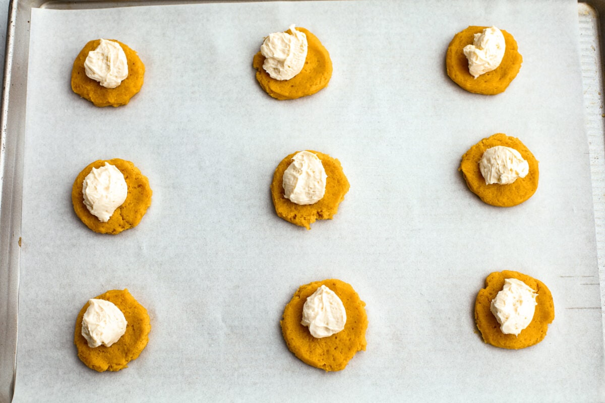 Pumpkin cheesecake snickerdoodle dough balls flattened with cream cheese on a baking sheet with parchment paper.  