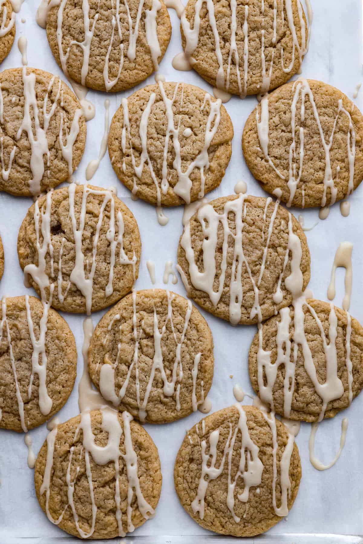 Apple cider cookies on parchment paper drizzled with a white glaze. 