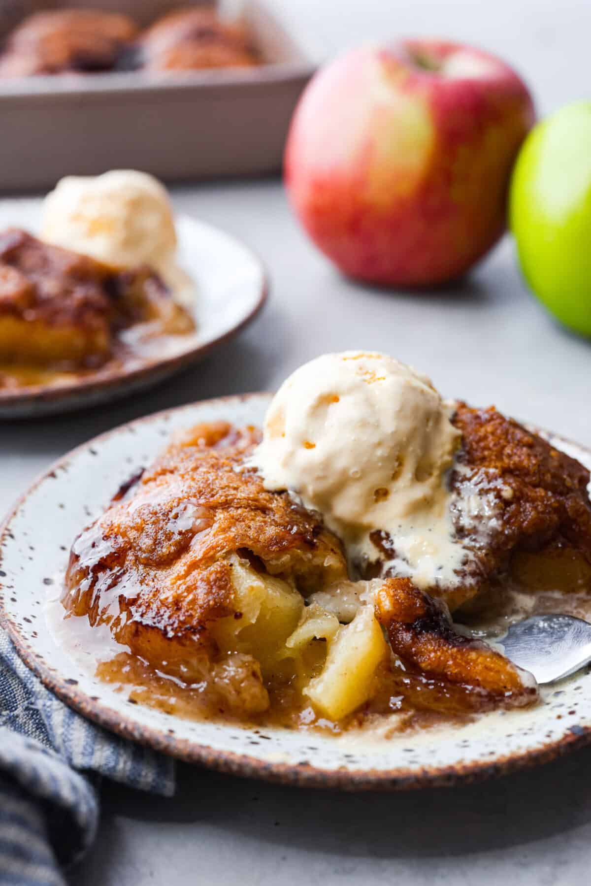 Baked apple dumplings on a white speckled plate with a scoop of vanilla ice cream on top.