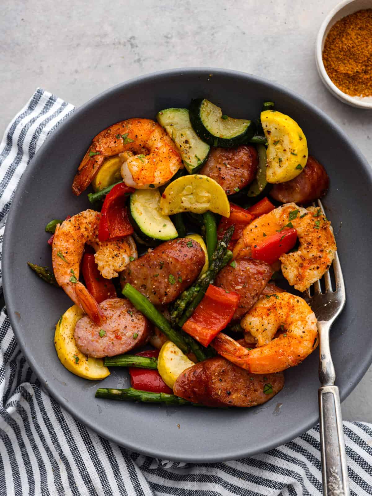 Close view of Cajun shrimp, sausage, and veggies in a gray bowl with a fork.