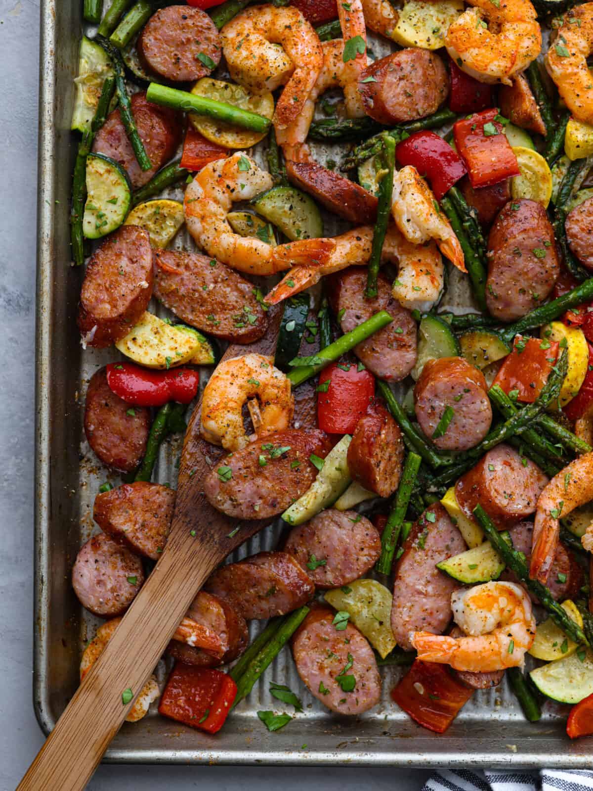Close view of cajun shrimp and sausage vegetable sheet pan with a wood serving spoon on the pan.