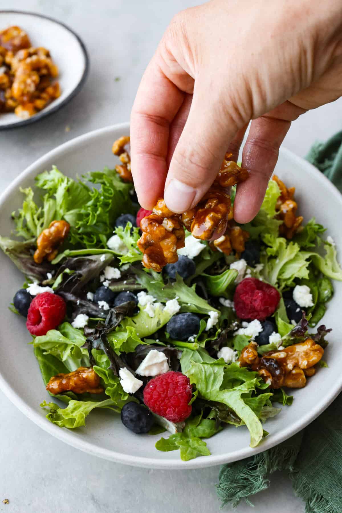 A salad being sprinkled with candied walnuts. 
