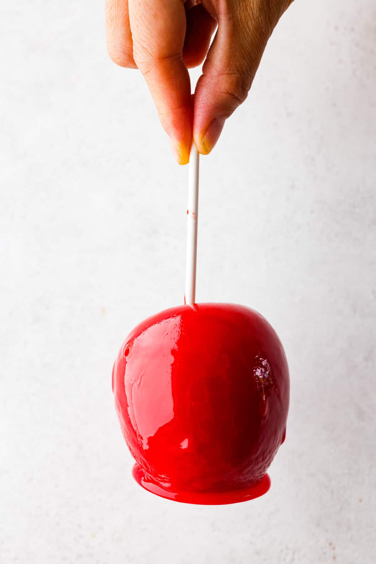 A whole candied apple being picked up by the stick.