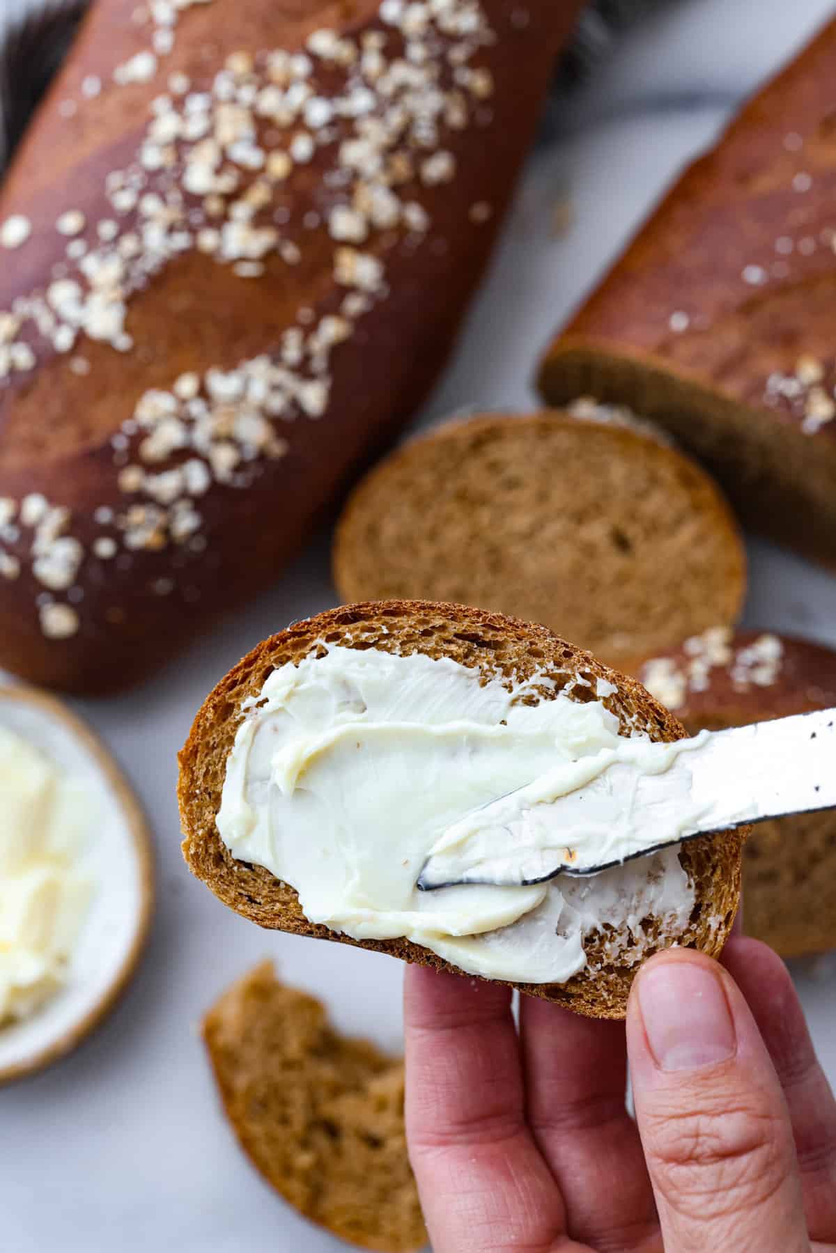 Close view of butter being spread onto a slice of brown bread.