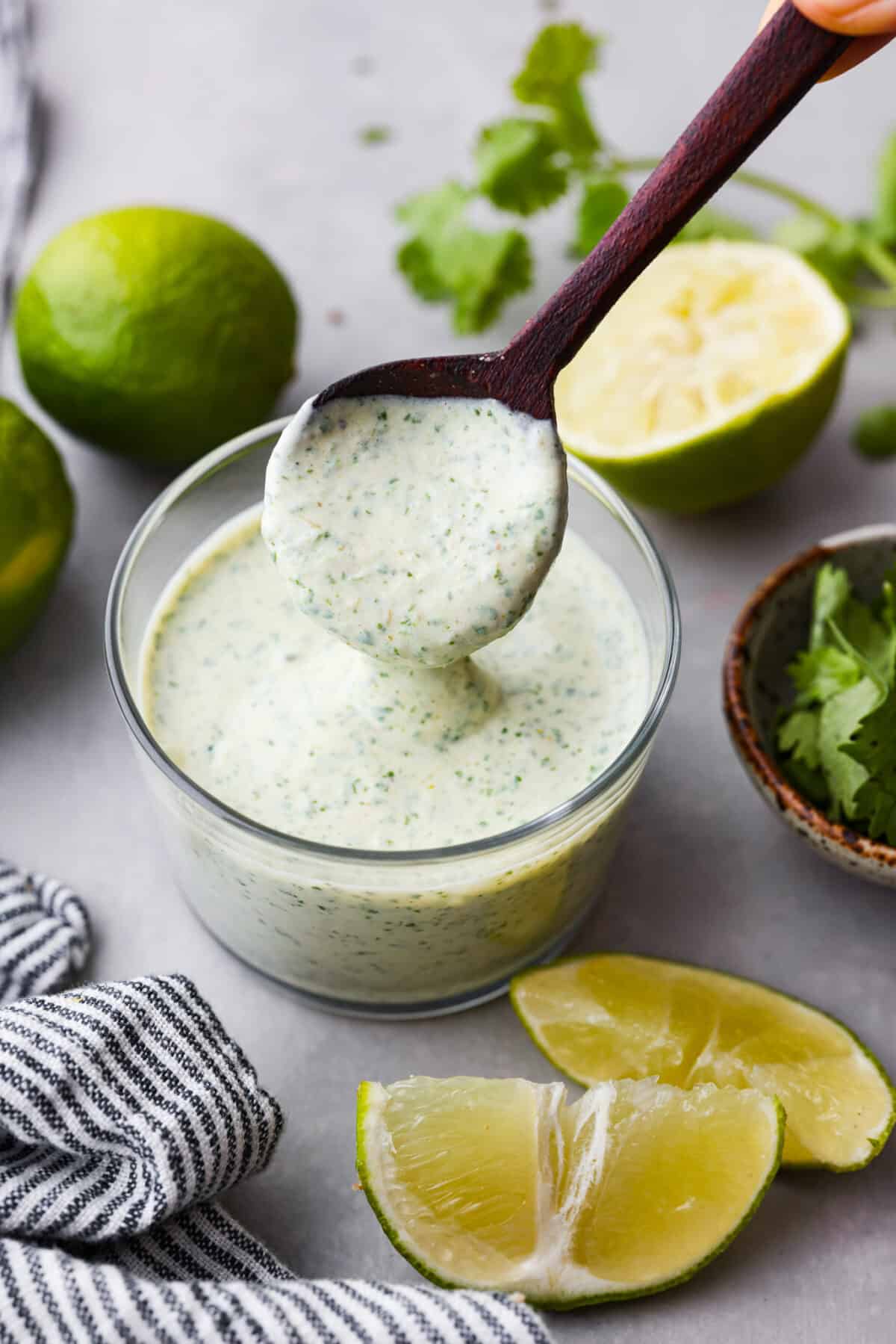 Hero image of cilantro lime sauce in a glass jar, being mixed with a wooden spoon.