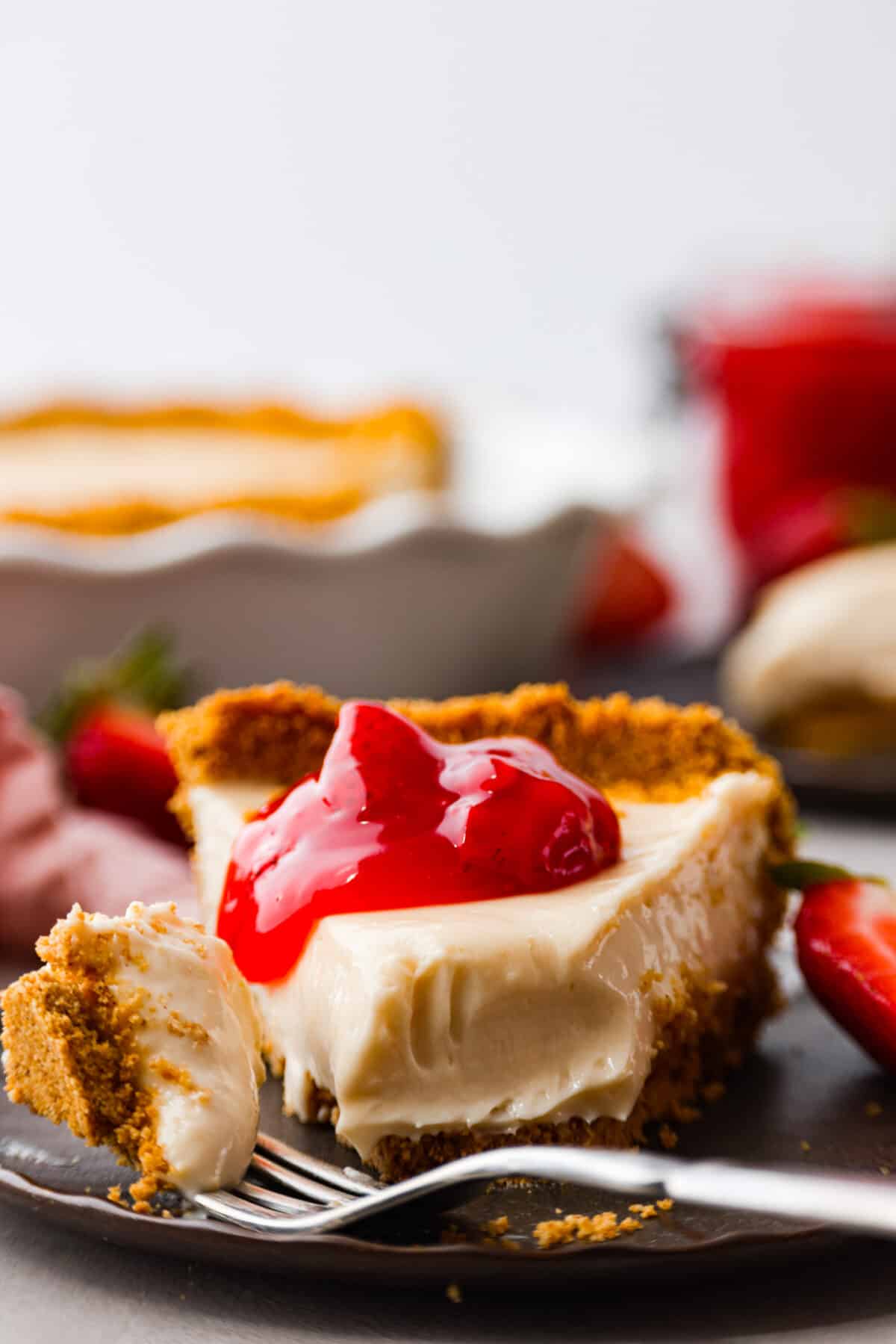 A slice of cream cheese pie with a dollop of strawberry pie filling on top. 