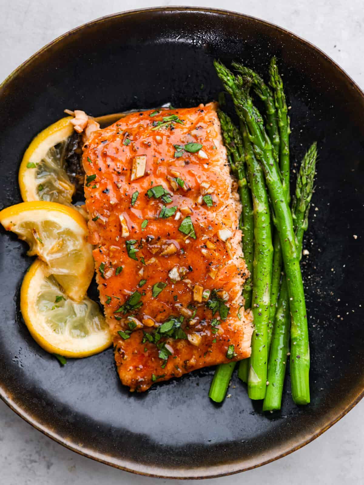 A woebegone plate with garlic brown sugar salmon, lemon slices and asparagus. 