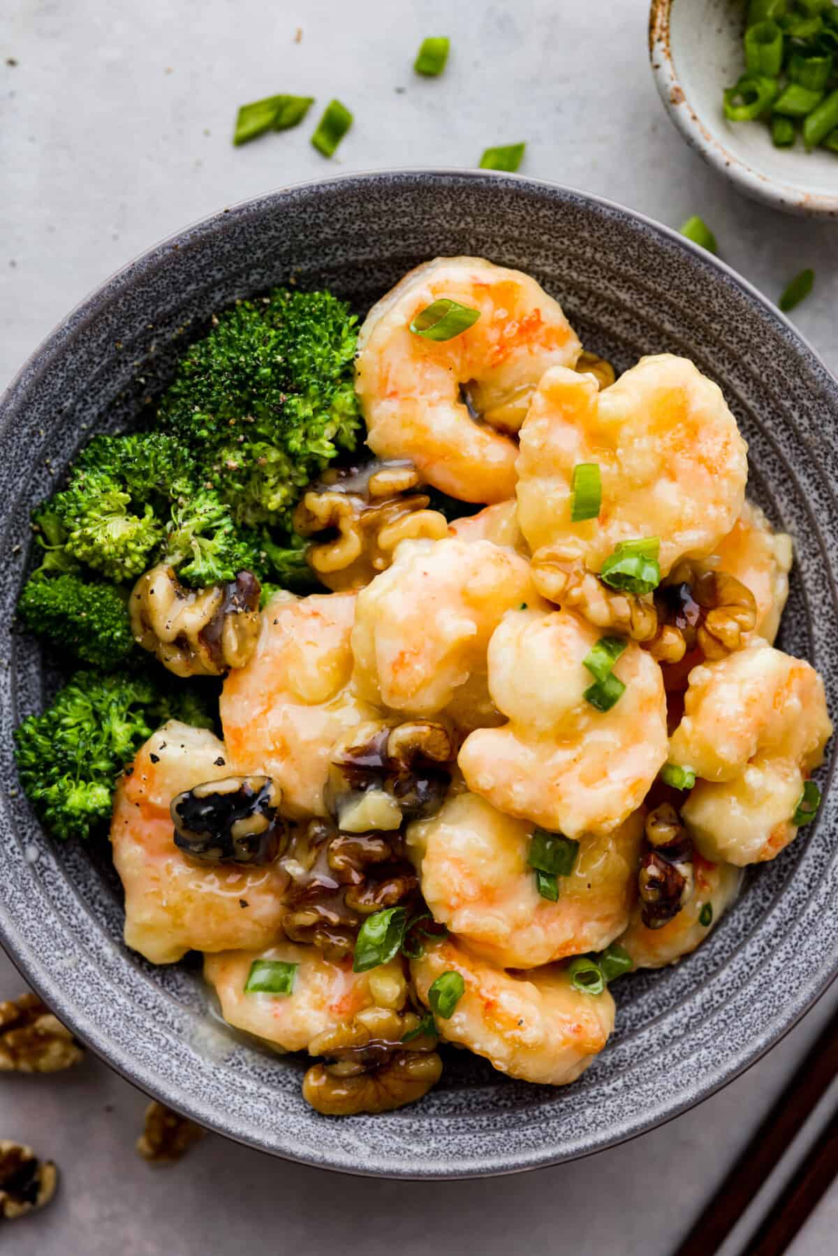 Crispy shrimp tossed in a creamy sweet sauce with candied walnuts. This honey walnut shrimp is so much better than takeout and one of the best shrimp recipes that you will make! Shrimp served with broccoli in a gray bowl.