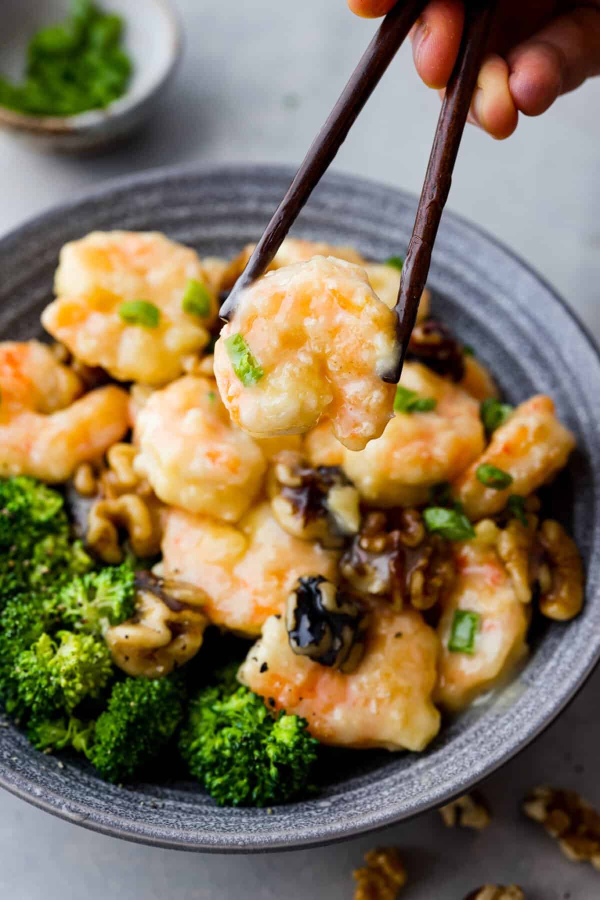 Crispy shrimp tossed in a creamy sweet sauce with candied walnuts. This honey walnut shrimp is so much better than takeout and one of the best shrimp recipes that you will make! Picking up a piece of honey walnut shrimp with chopsticks.