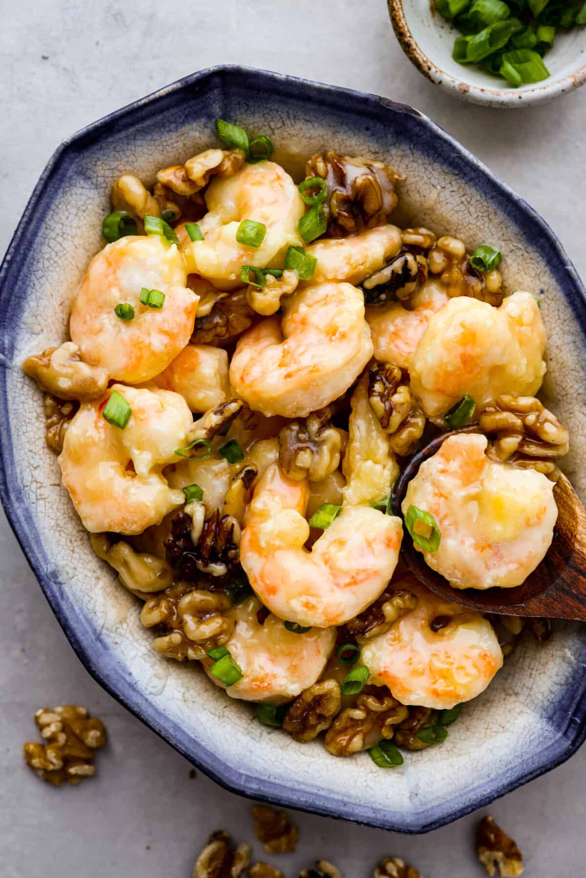 Crispy shrimp tossed in a creamy sweet sauce with candied walnuts. This honey walnut shrimp is so much better than takeout and one of the best shrimp recipes that you will make! Hero image of crispy walnut shrimp on a blue and white serving dish.
