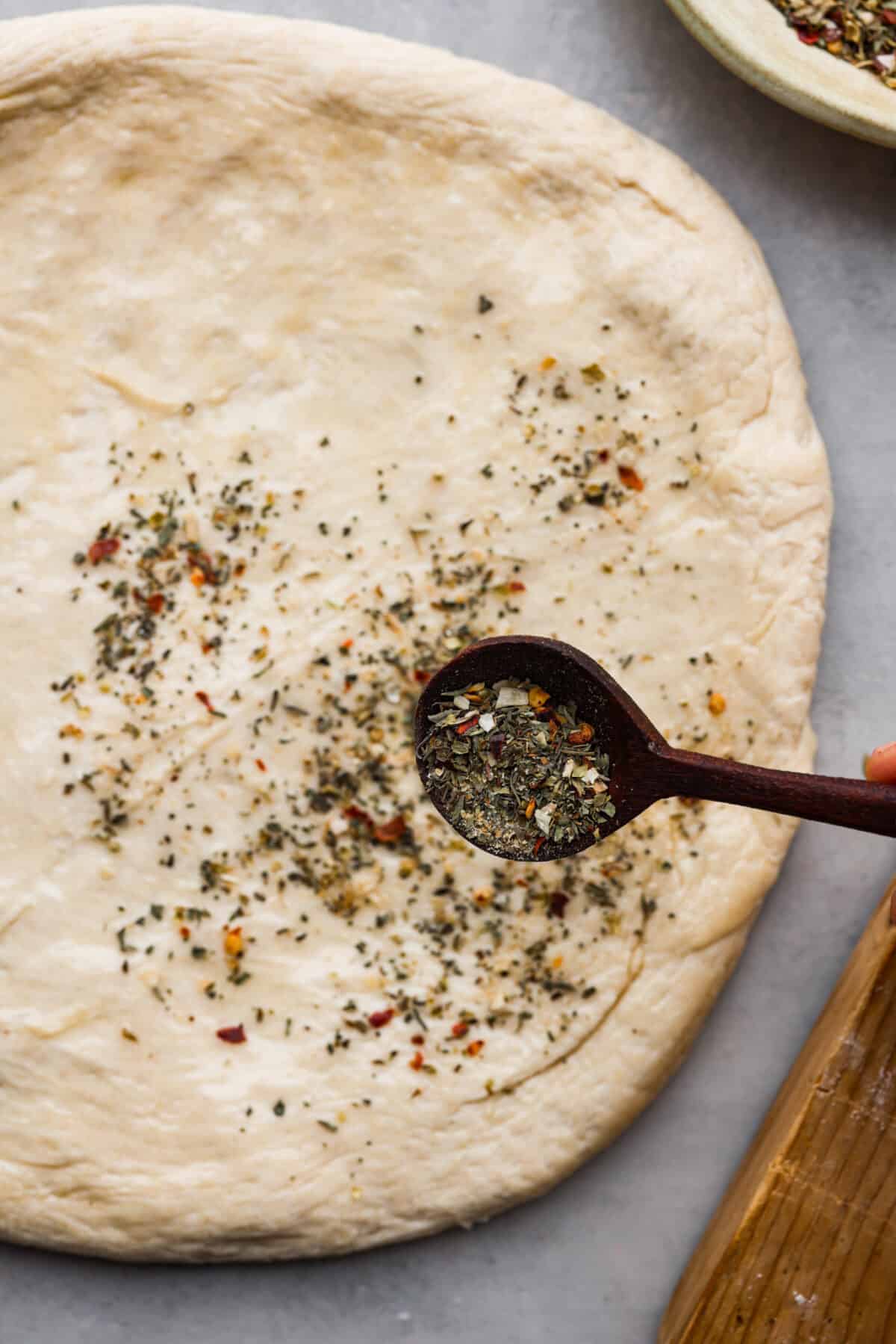 Pizza seasoning being sprinkled over dough.