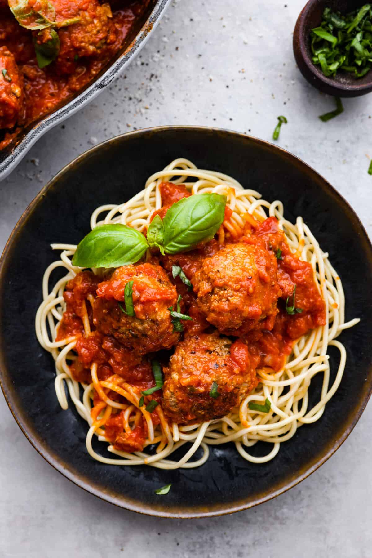Top view of ricotta meatballs on a bed of spaghetti noodles in a black bowl.