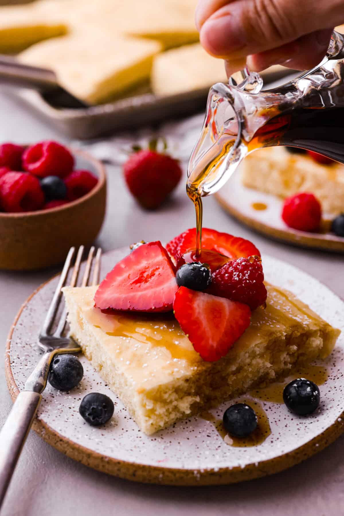 A sheet pan pancake slice topped with syrup and fruit.