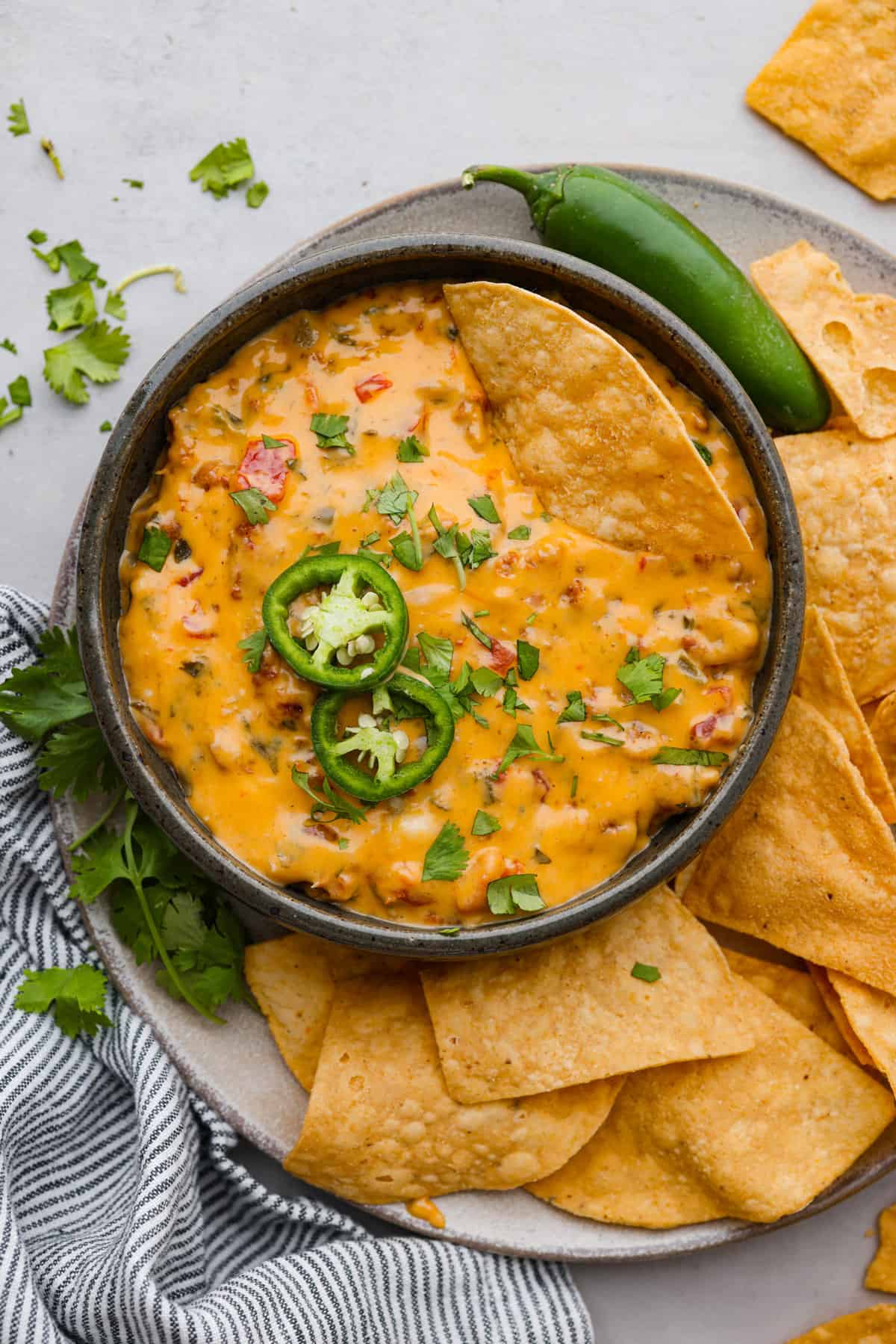 Top view of smoked queso dip in a black bowl on top of a serving platter. Chips and cilantro surround the bowl with a chip resting in the dip.