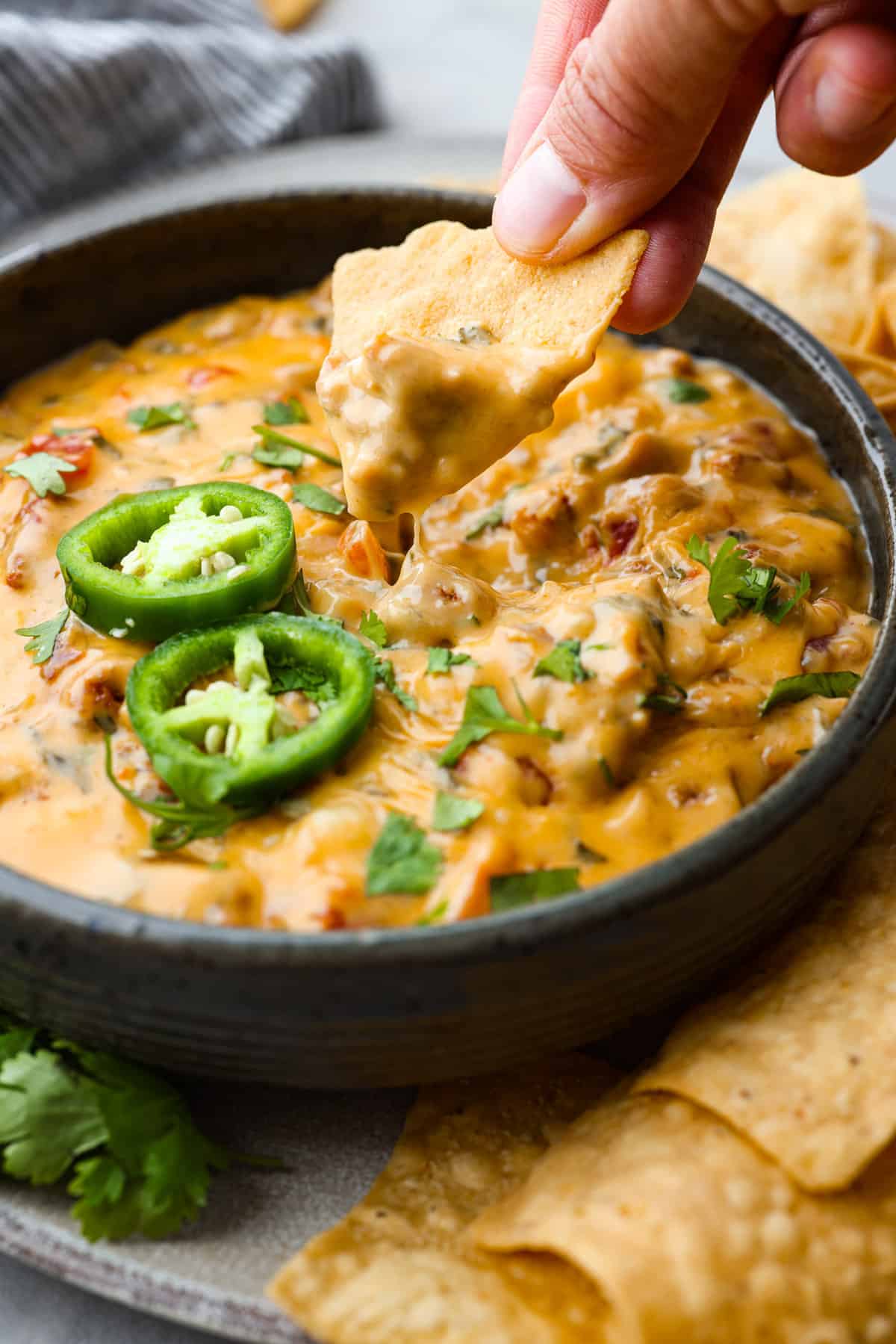 Close view of smoked queso dip in a black bowl with a chip scooping up dip.