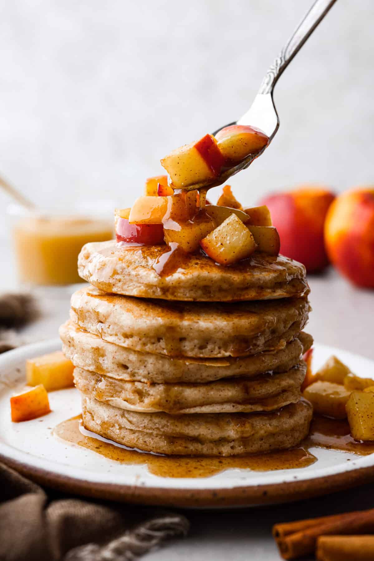 Close view of a stack of applesauce pancakes with a spoon placing sauteed apples on top.