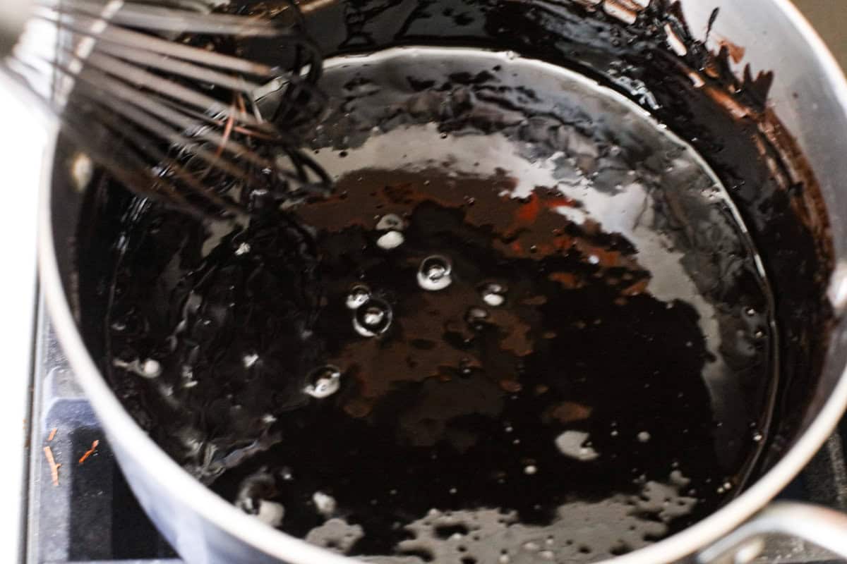 This delicious black frosting is fun to make for special occasions, especially for Halloween, seasonal treats, and desserts. It's made with black cocoa powder, which tastes just like Oreo's! The best part is that it won't dye your mouth, hands, or clothing! It's the perfect frosting for witchy cakes and other dramatic parties. Overhead shot of the milk and sugar mixture in a pan, cooking on the stove top.