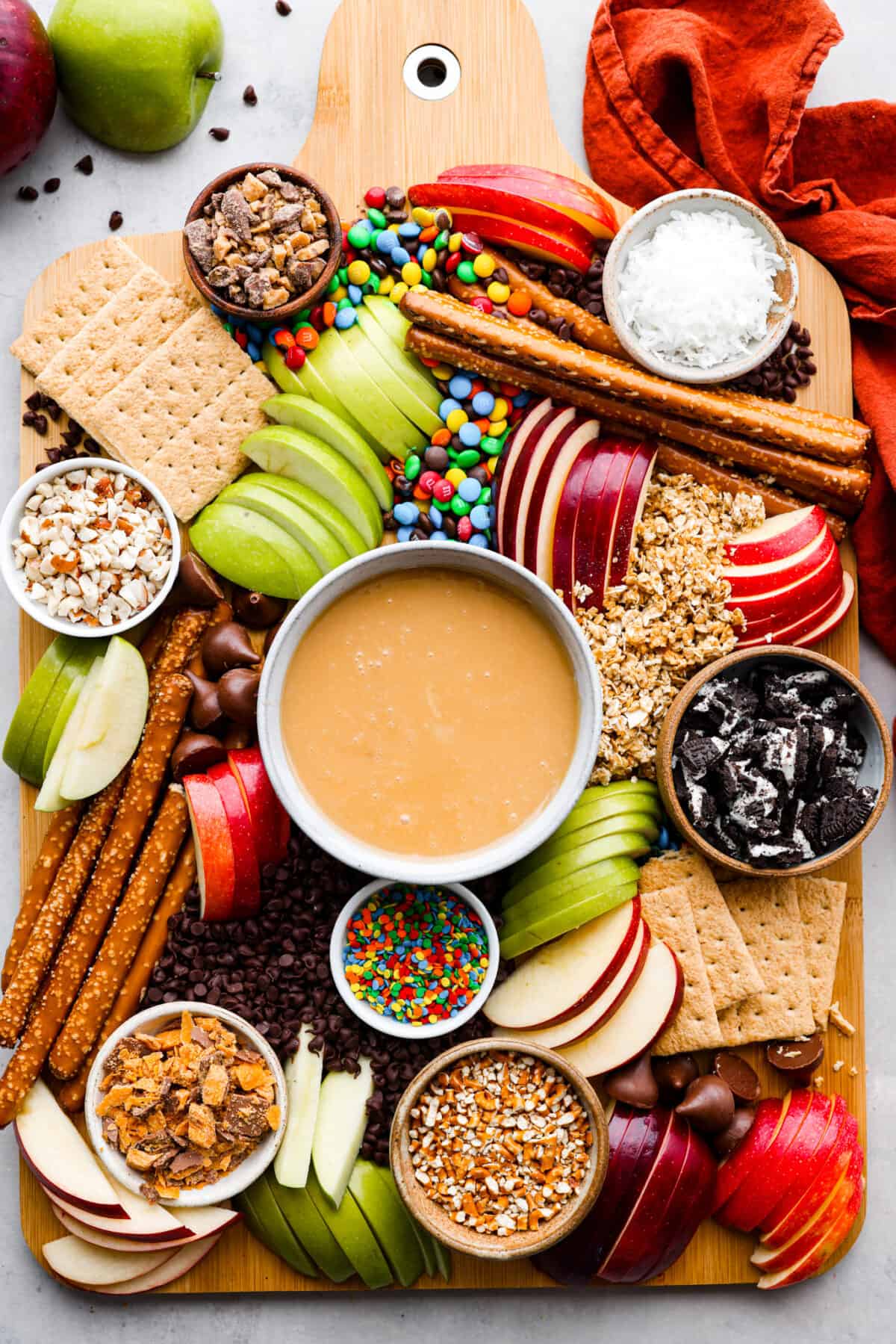 Top-down view of a whole caramel apple charcuterie board, filled with various cookies, candy, pretzels, crackers, and apple slices.