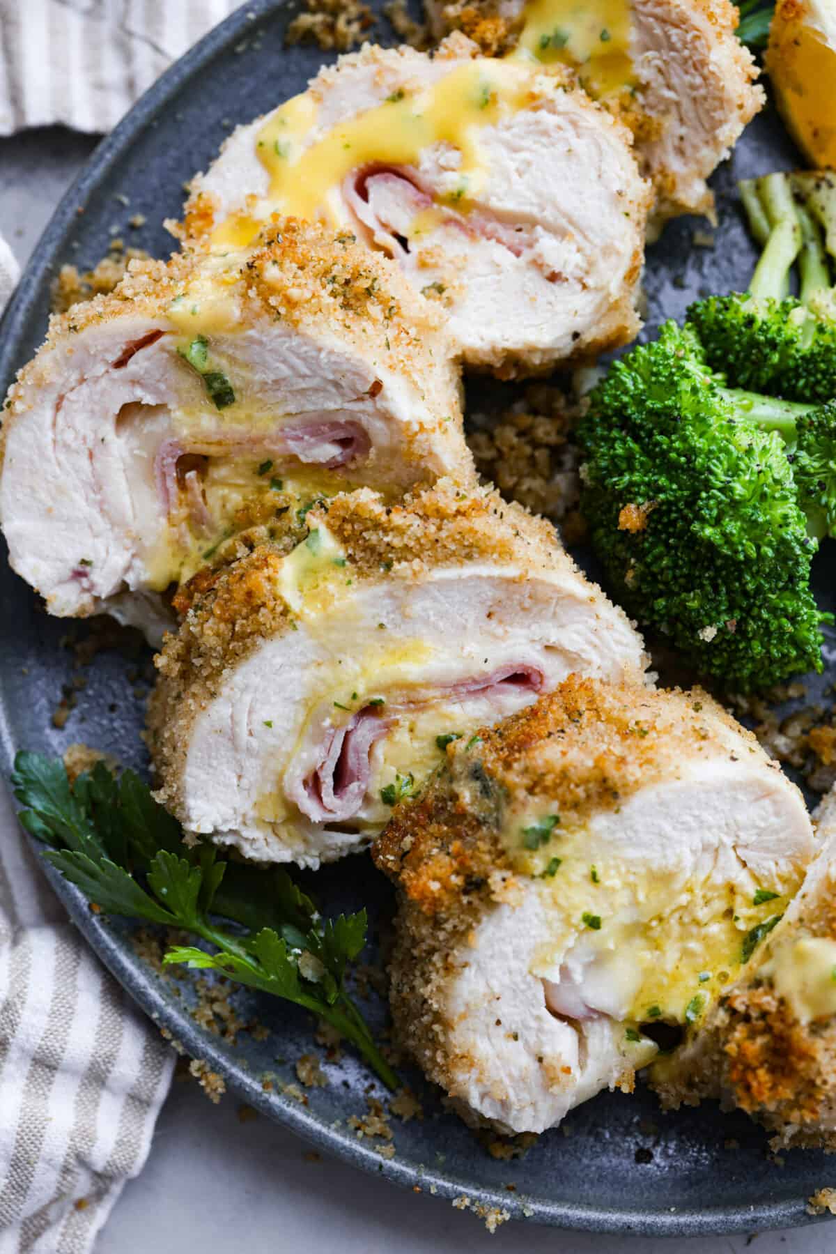 Top view of sliced chicken cordon bleu on a gray plate drizzled with sauce and broccoli on the side.