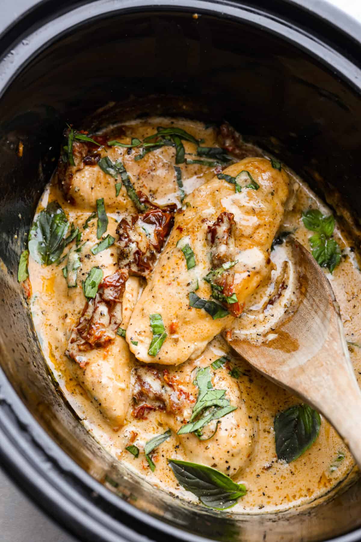 Cooked Tuscan chicken in a crock pot, garnished with fresh basil.