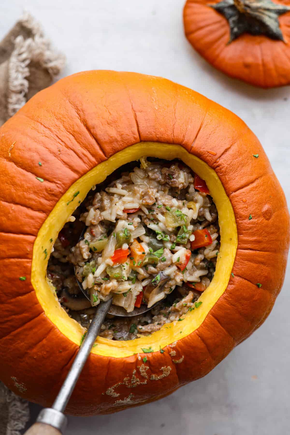 Top-down view of a pumpkin that has been hollowed out and filled with sausage, rice, and vegetables.