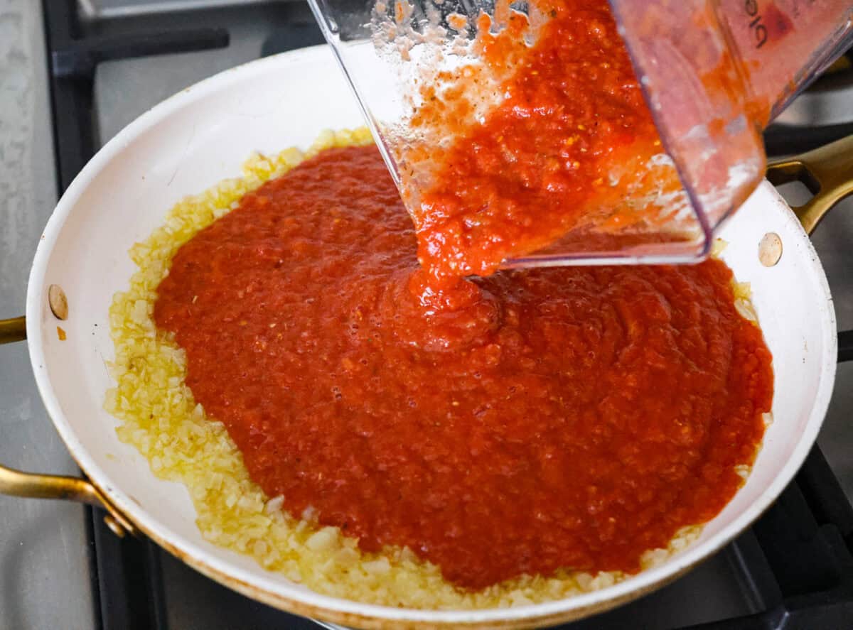 Blended up ingredients being added to the onions in the saucepan. 