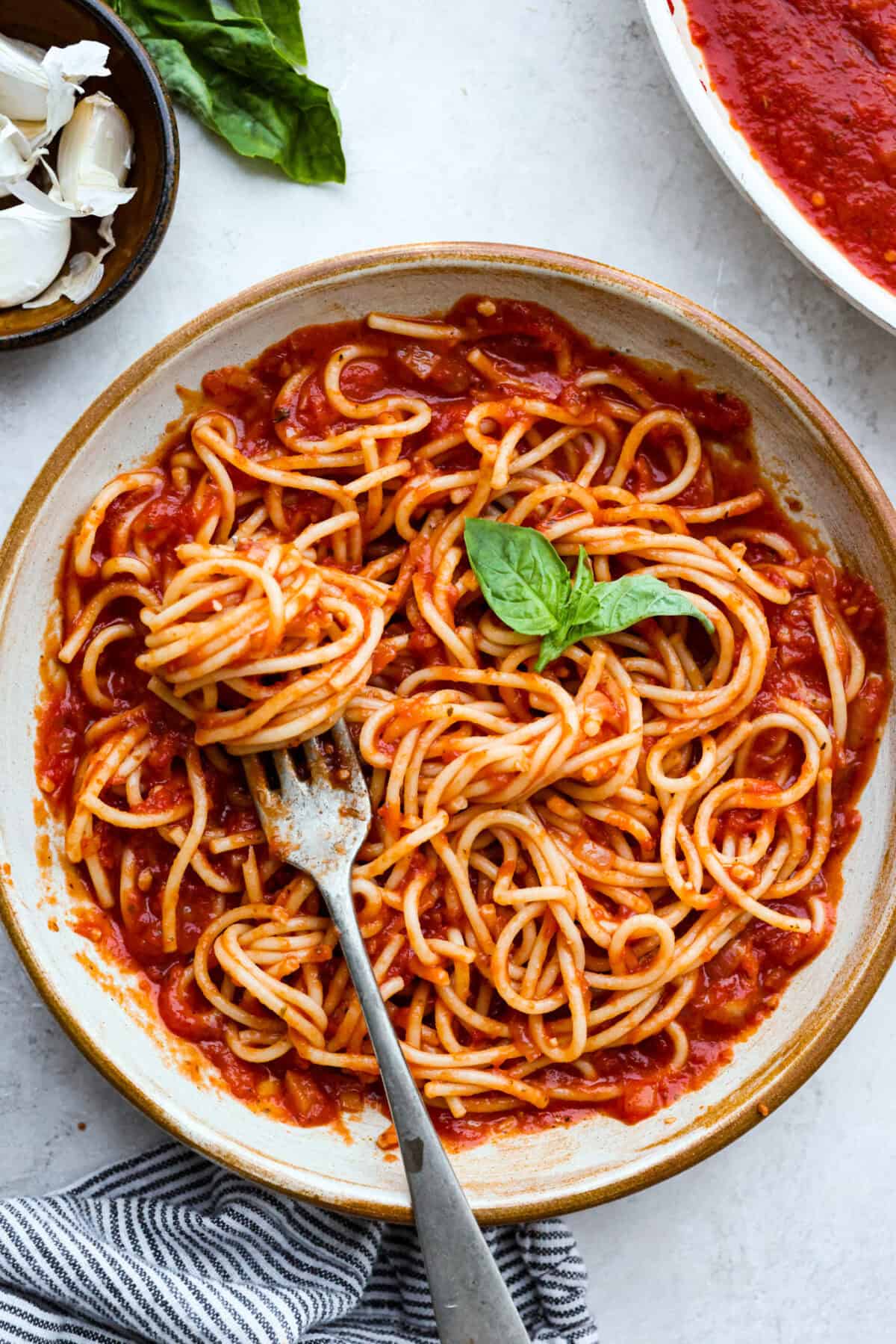 Plate of spaghetti noodles smothered in homemade marinara sauce garnished with a sprig of fresh basil. 