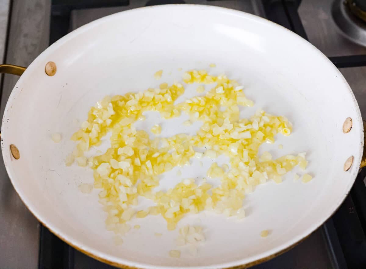 Onions sautéing in olive oil in a skillet on the stovetop. 