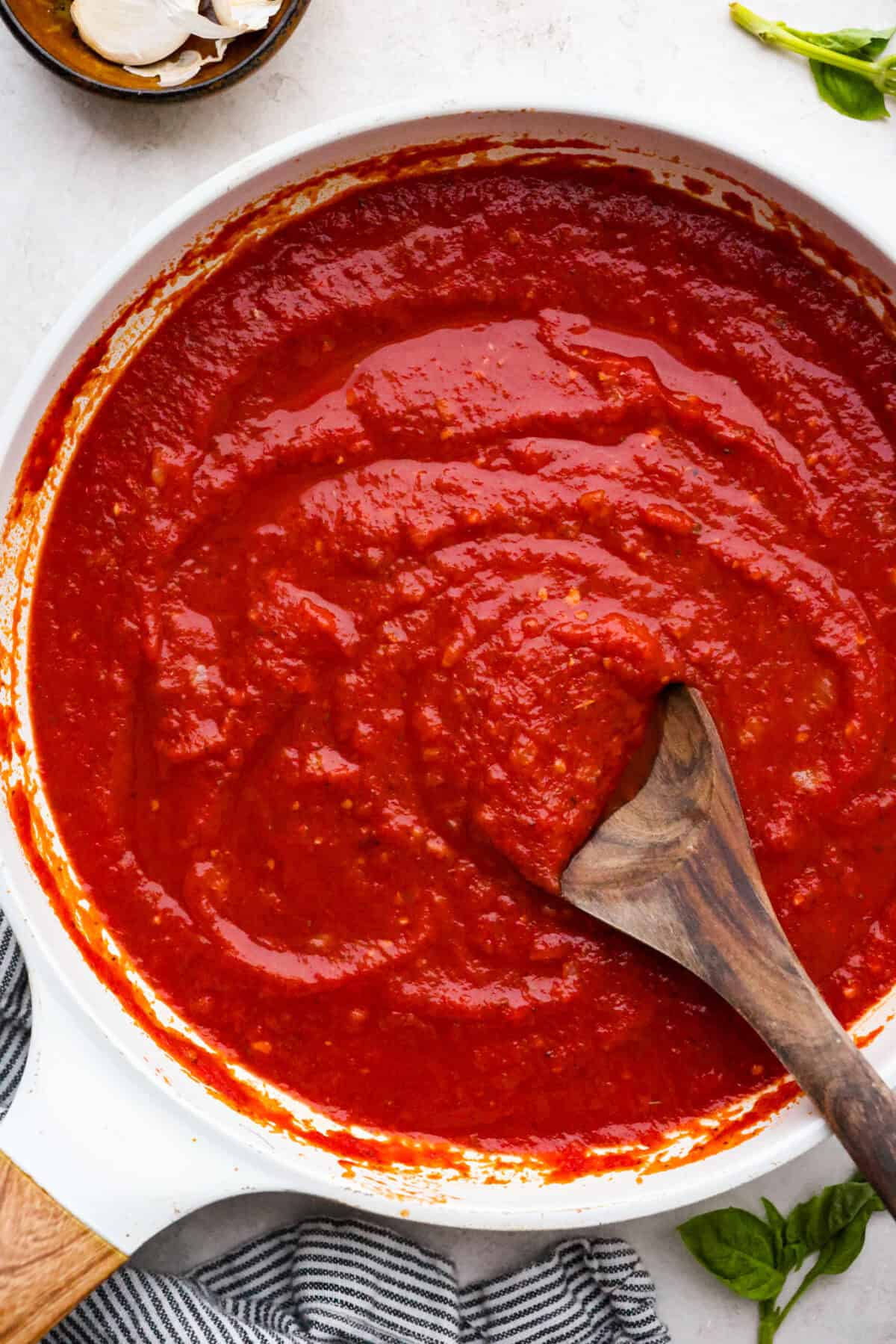 Top down shot of homemade marinara sauce in a saucepan with wooden serving spoon. 