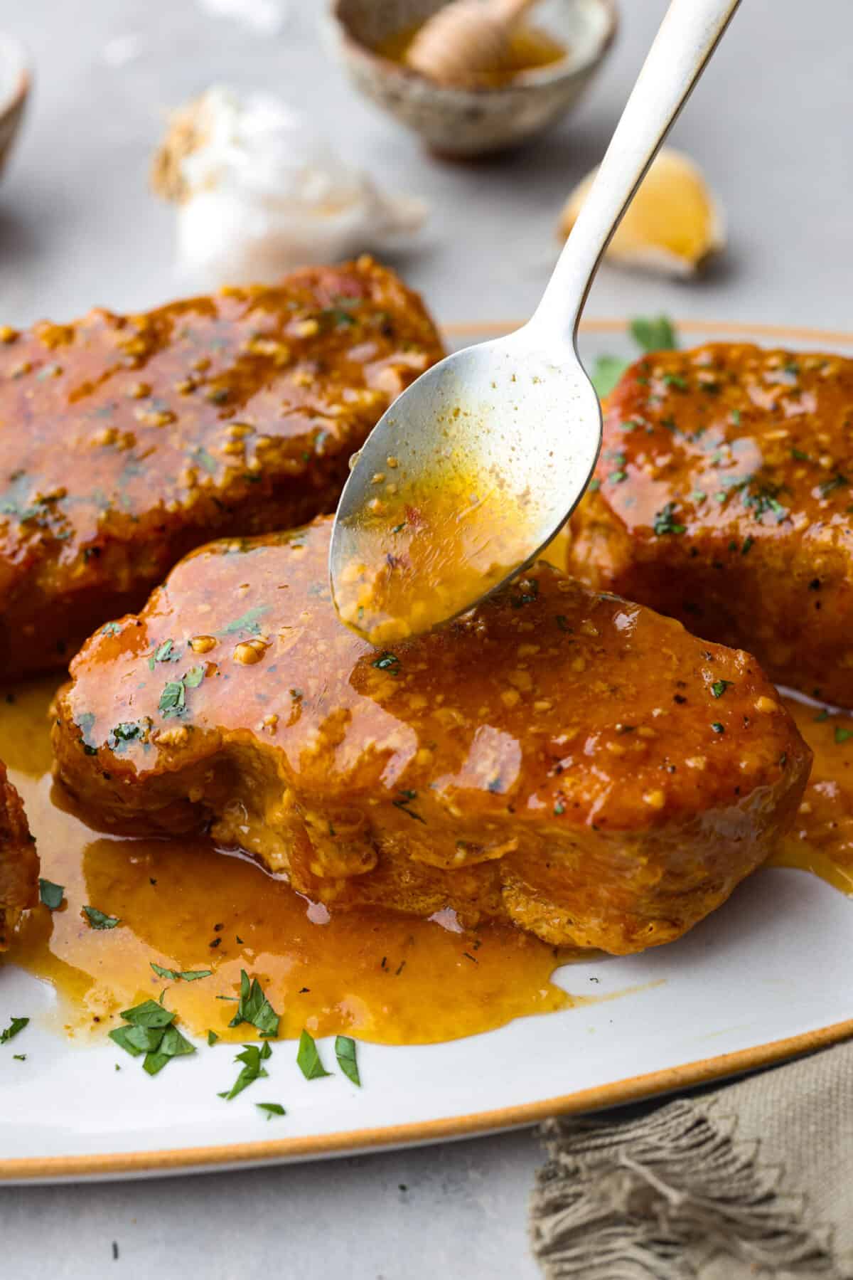 Spooning honey garlic sauce over a pork chop.