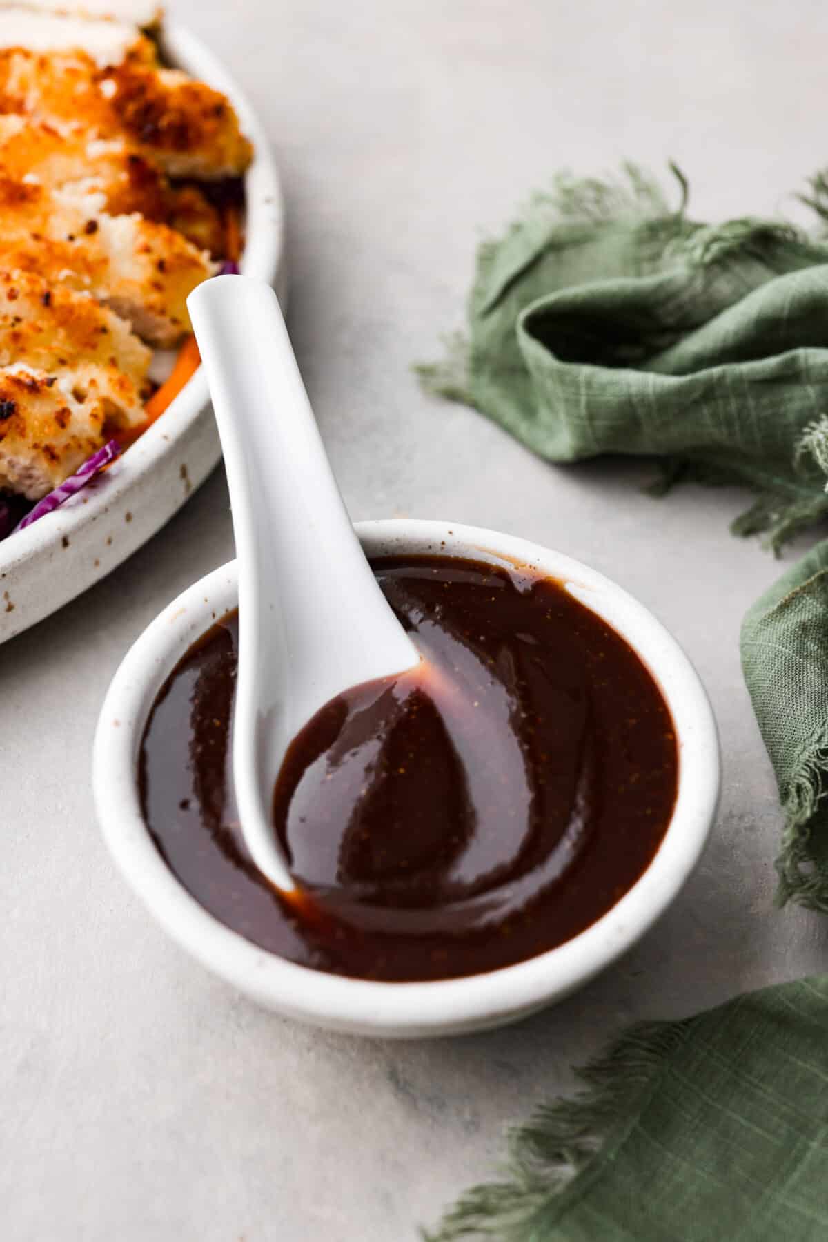 A large white spoon inside a small bowl of katsu sauce.