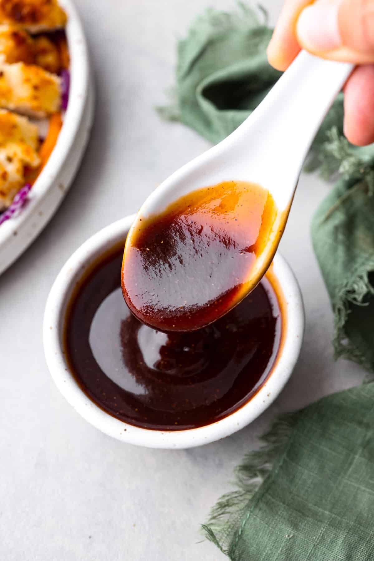 A small white bowl filled with homemade katsu sauce, being served with a large soup spoon.