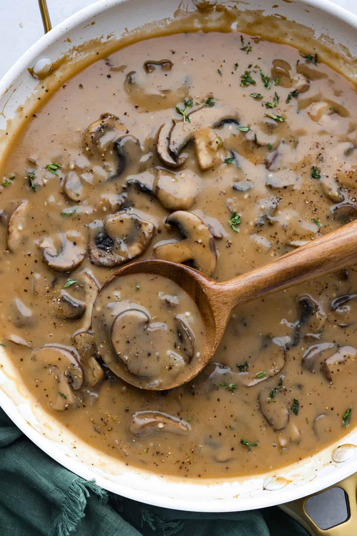 Mushroom gravy in a white skillet, being stirred with a wooden spoon.