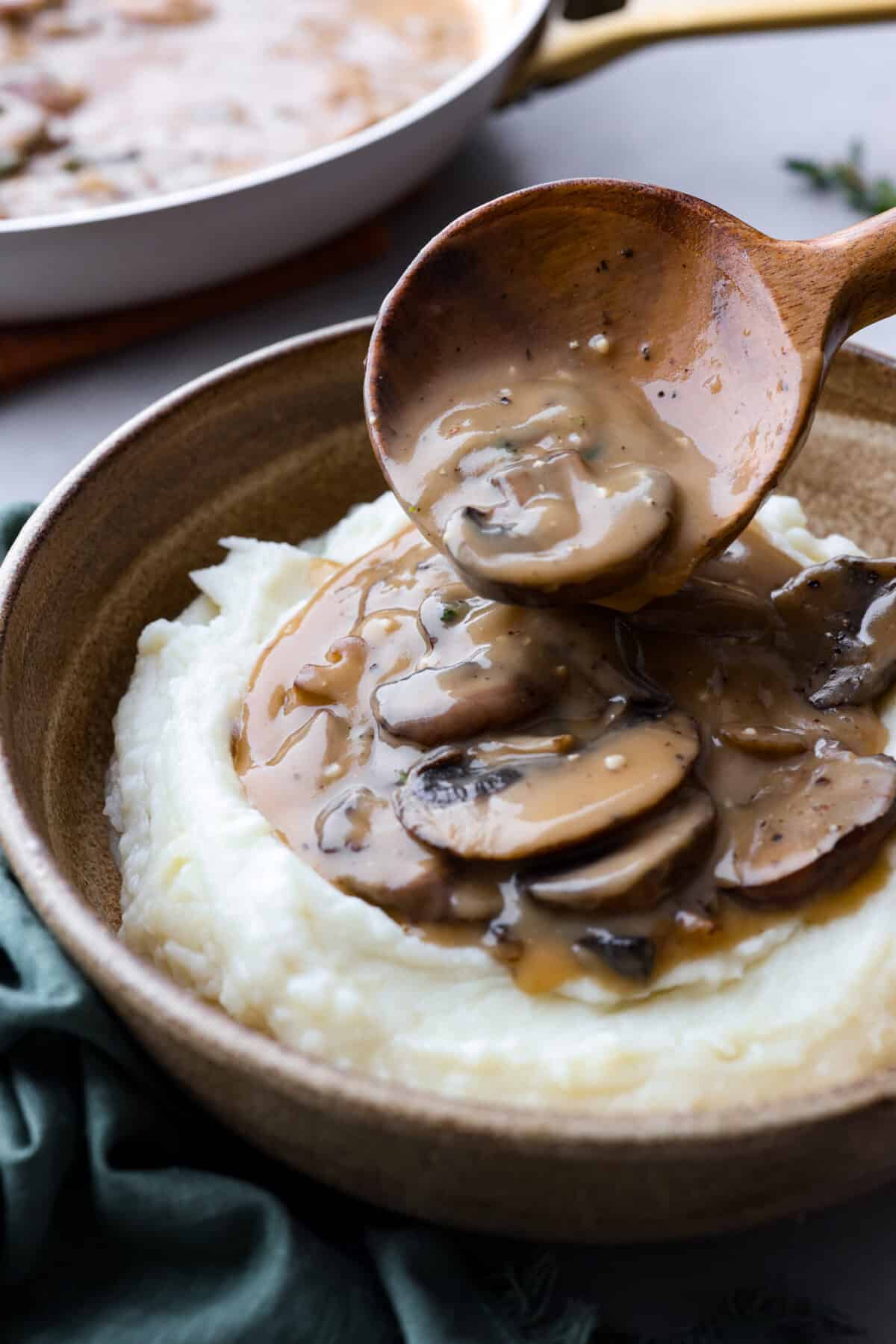 Mushroom gravy being poured over a serving of mashed potatoes.