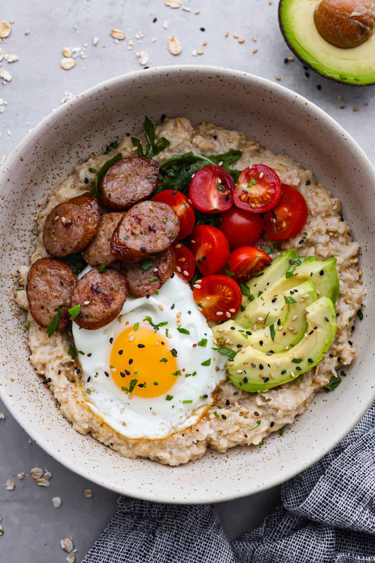 Savory oatmeal topped with a fried egg, tomatoes and chicken sausage.