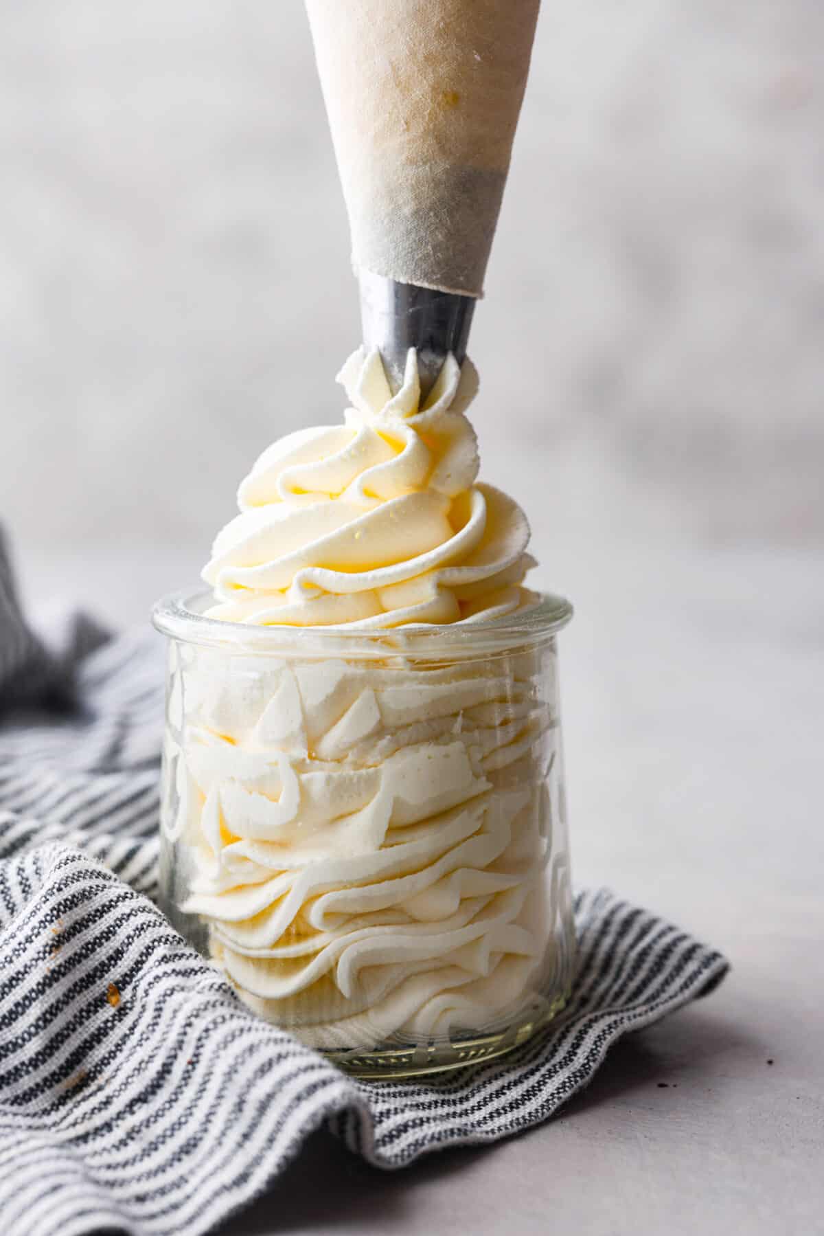 Side view of a piping bag piping stabilized whipped cream into a glass jar.