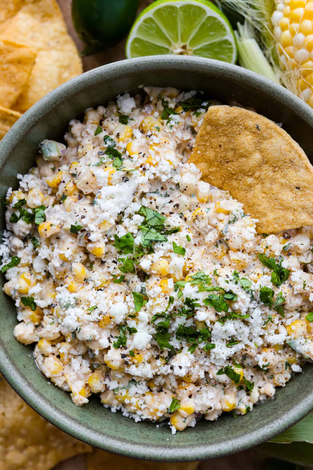 A close up of a bowl of corn dip with a tortilla chip in it. 