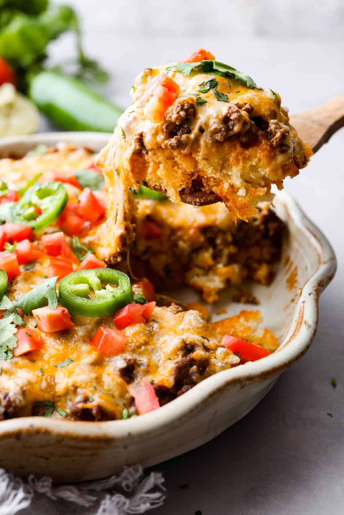 Tamale Pie being scooped out of a casserole dish with a wooden spoon. 