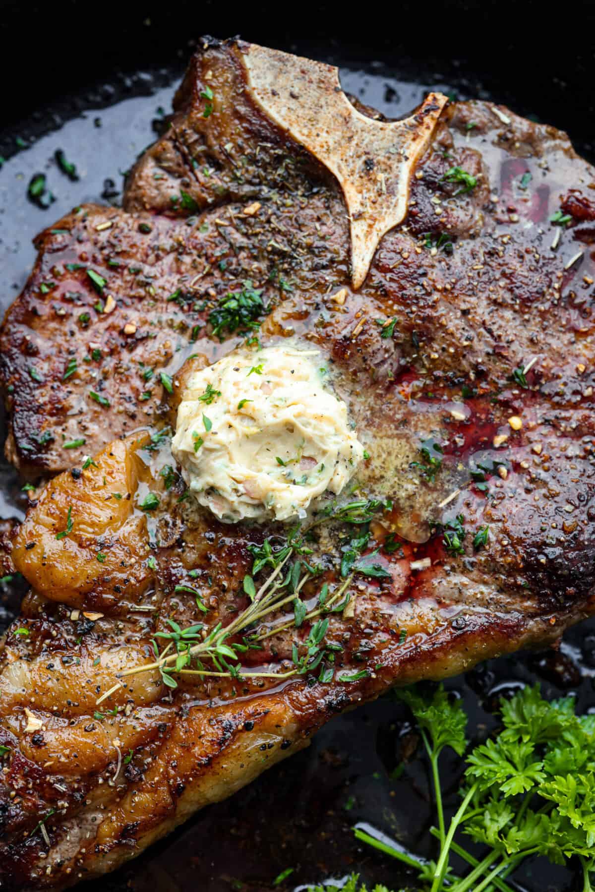 Top-down view of steak topped with butter and herbs.